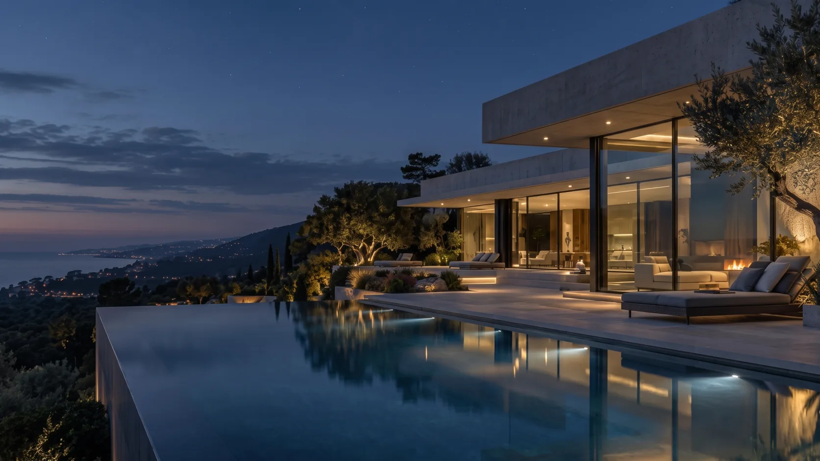 Contemporary coastal estate with warm illuminated interiors and an infinity pool at dusk